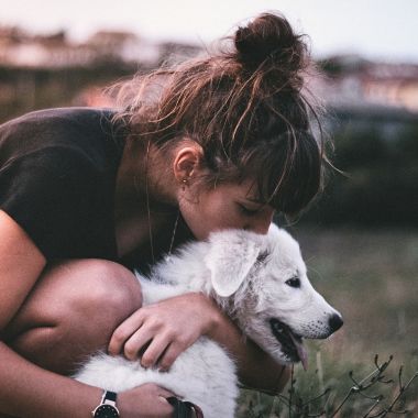 woman kissing and hugging her white dog outdoors